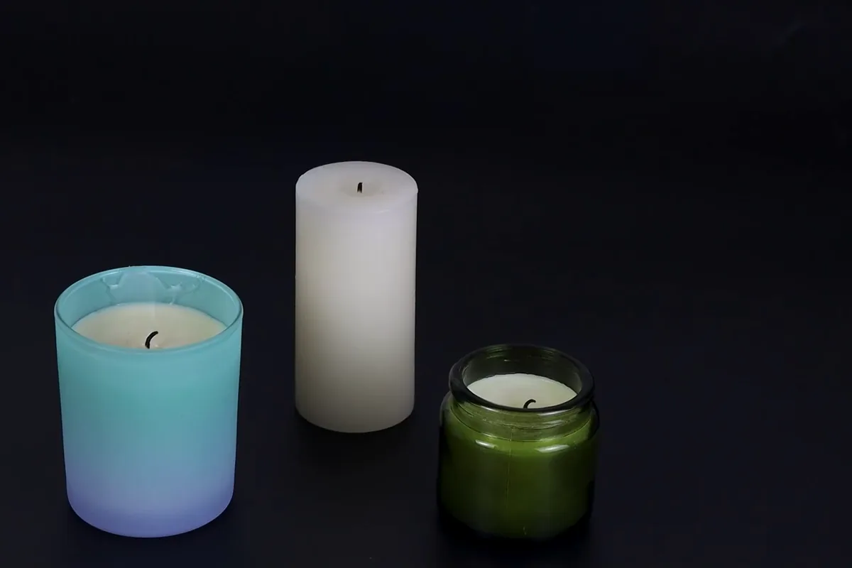Three candles on a dark table — a blue glass jar, a white pillar and a green jar — lit by a TOPKAY electric arc lighter